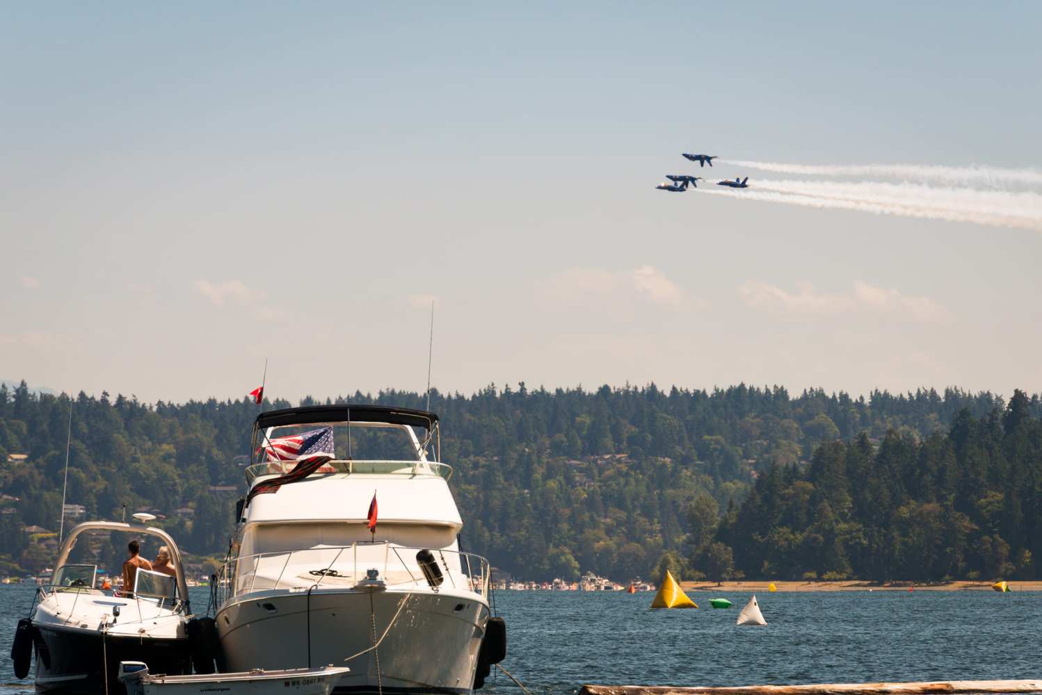 Four jets fly in formation over a lake with boats and distant treeline.