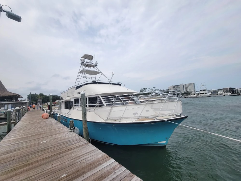 Docked boat with blue hull on a cloudy day, near buildings.