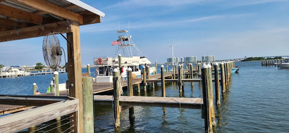 Dock with boats on a sunny day, American flag on a boat, clear blue sky.